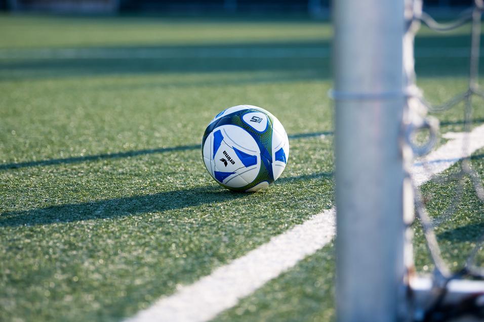 Fußball liegt auf einem Kunstrasenplatz, nahe einem Torpfosten mit Netz.