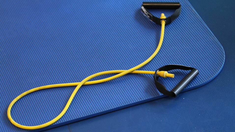 Gelbes Widerstandsband mit schwarzen Griffen auf einer blauen Gymnastikmatte.